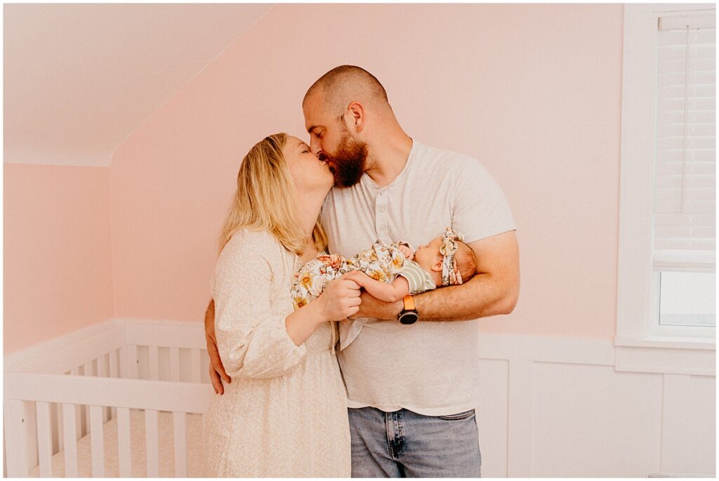 mom and dad holding baby kissing