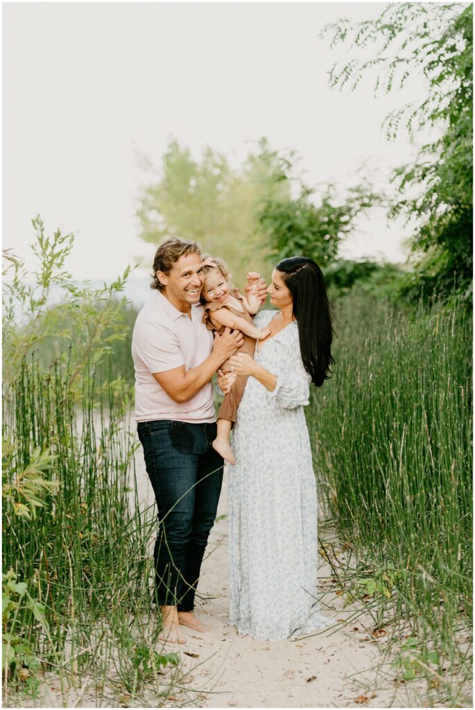 family holding little girl laughing on a beach