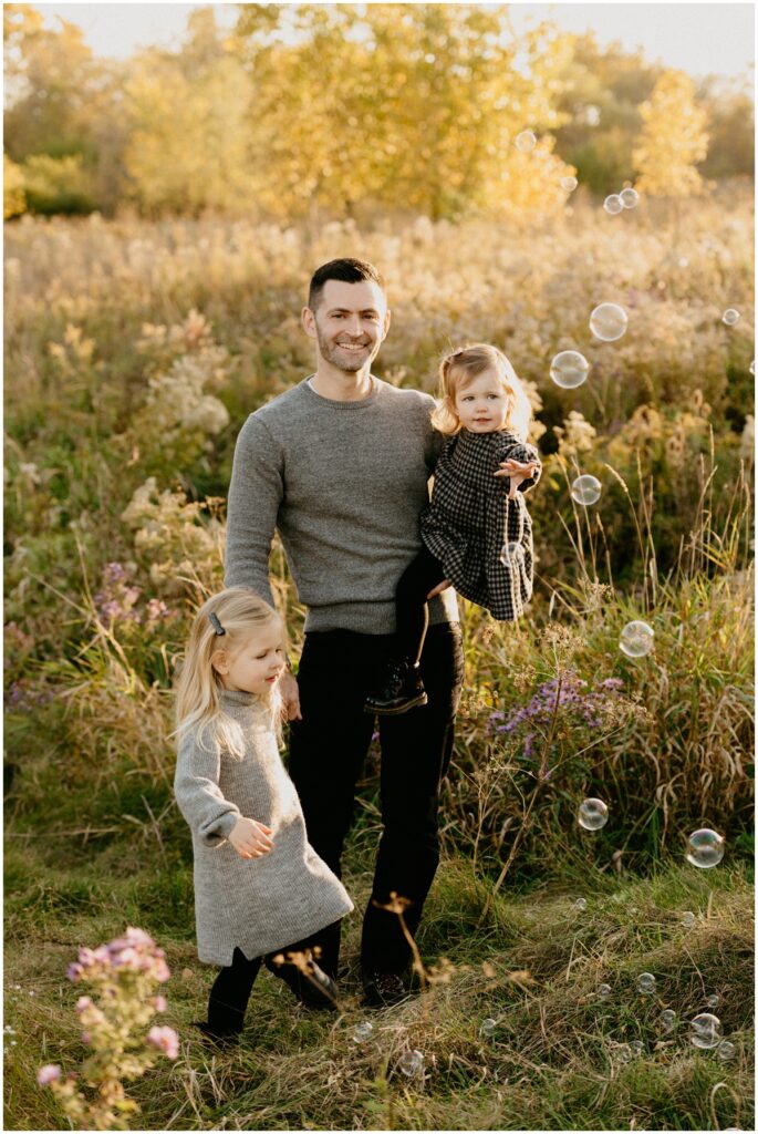 dad with two daughters at a park playing with bubbles