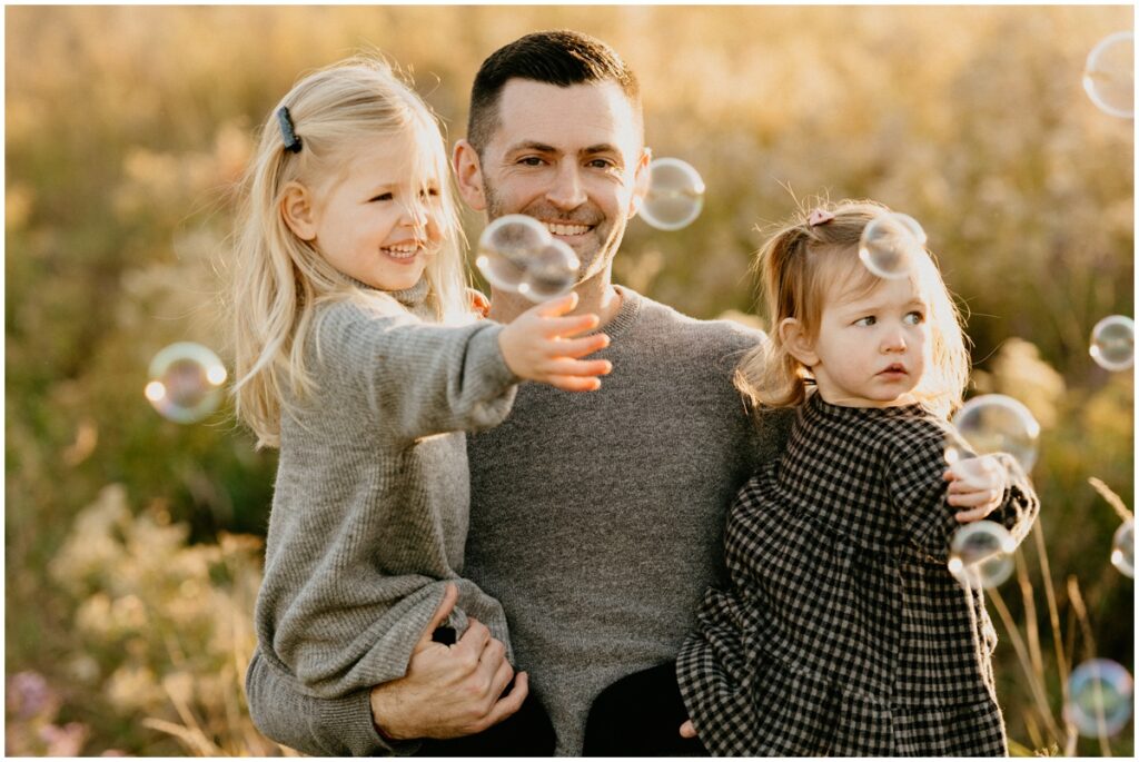 dad with two daughters at a park with bubbles