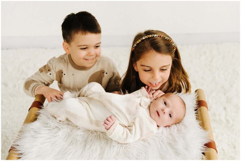 smiling siblings looking at smiling baby sister
