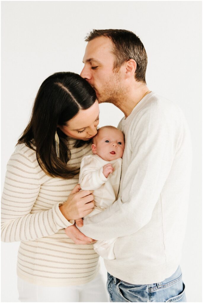mom and dad kissing with baby girl in the middle