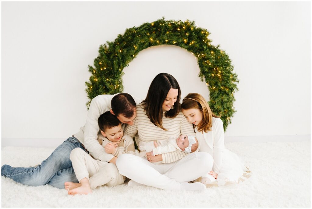 family photo in front of christmas wreath with newborn baby
