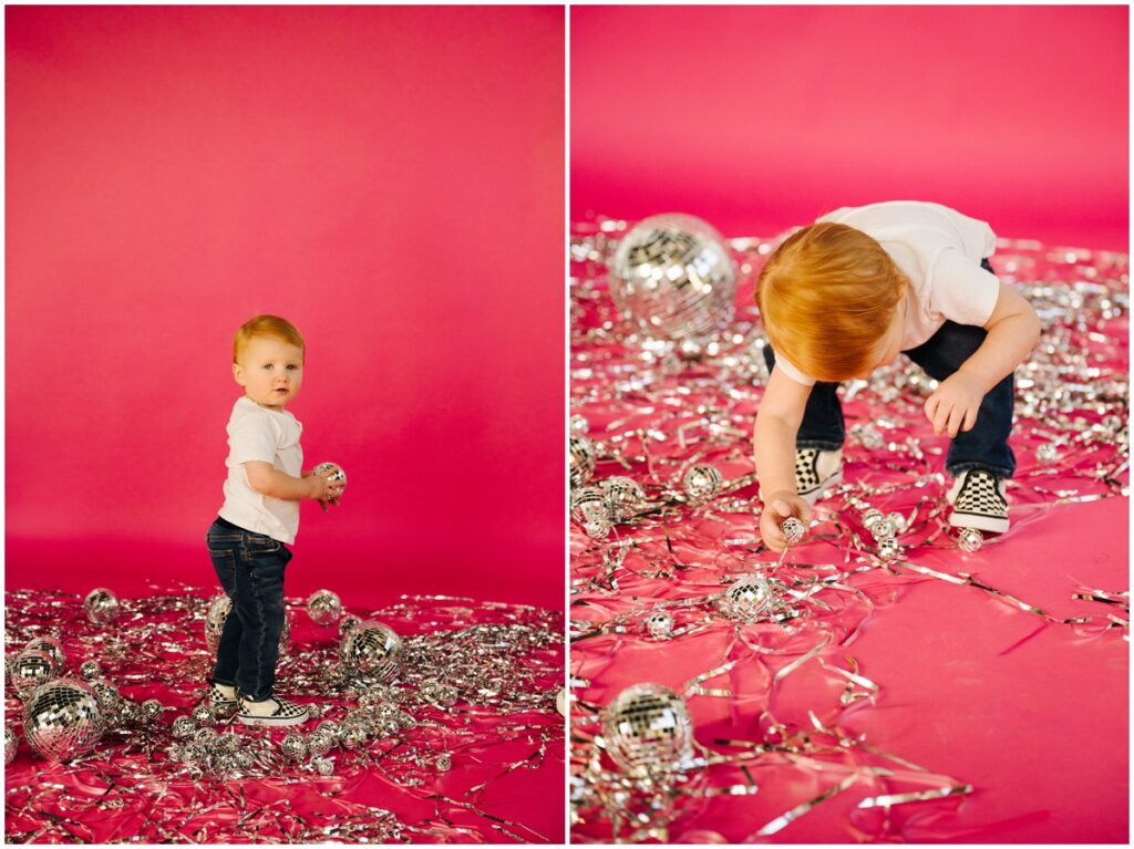little boy playing with silver decorations on pink background
