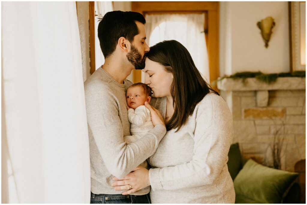 mom and dad kissing baby in middle