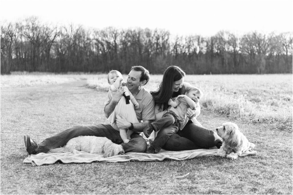 family photo outside with two dogs tickling kids