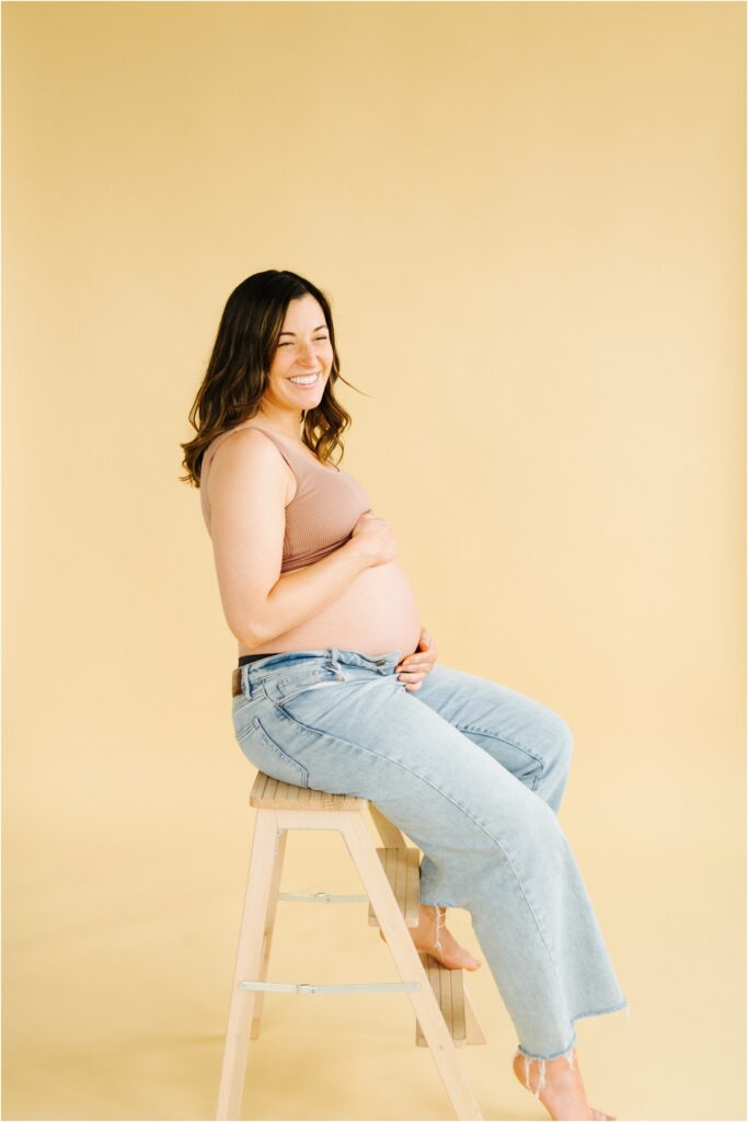 maternity photo of a woman on a beige backdrop laughing