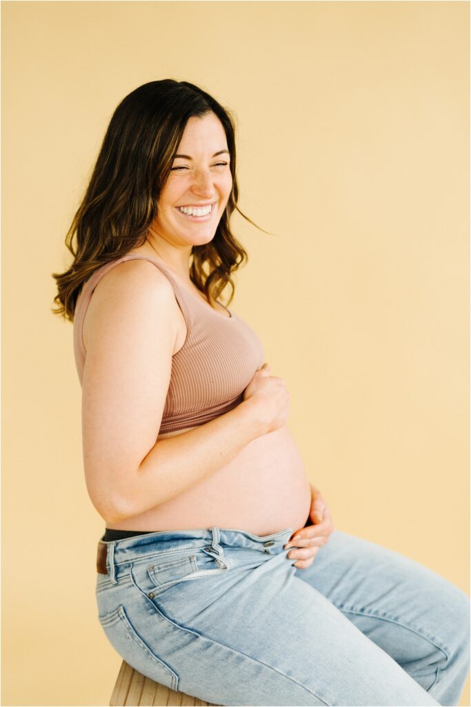 maternity photo of a woman on a beige backdrop woman smiling