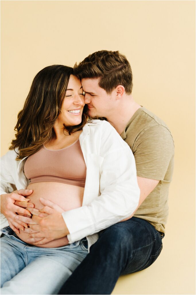maternity photo of a couple snuggling on a beige backdrop