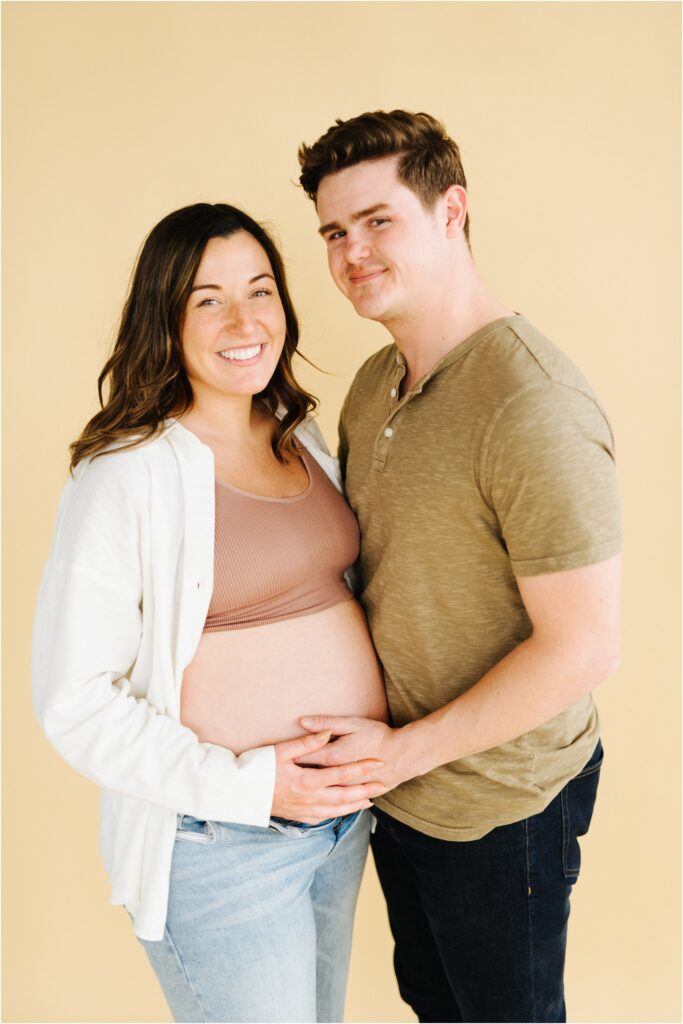 maternity photo of a couple looking at camera on a beige backdrop