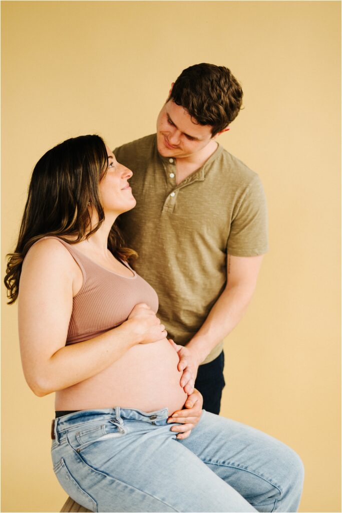 maternity photo of a couple looking at each other on a beige backdrop