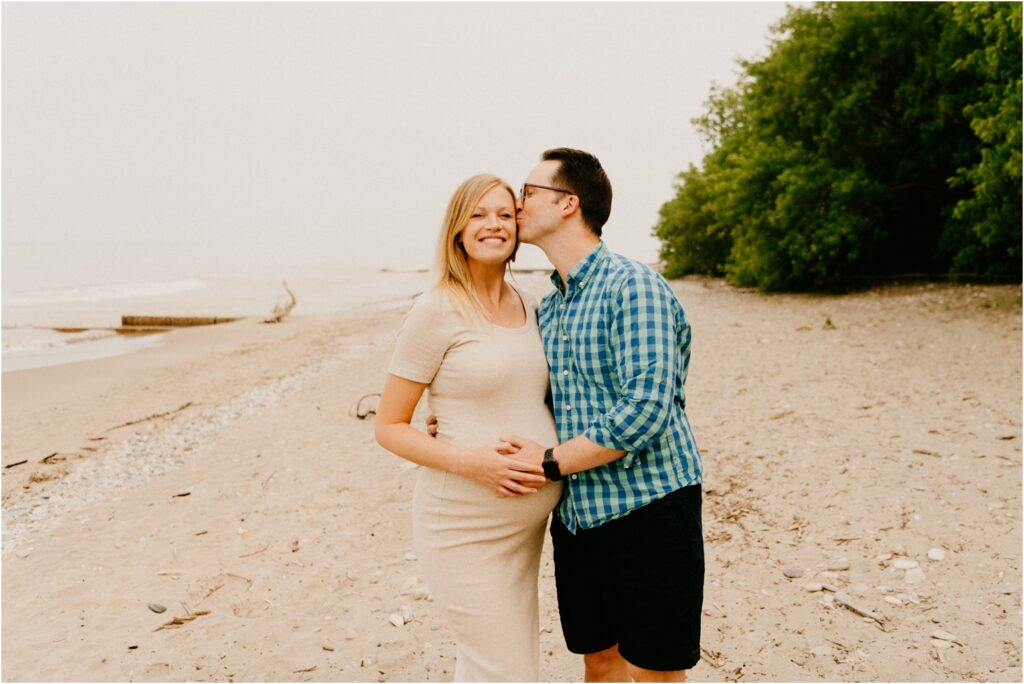 pregnant couple on the beach kissing