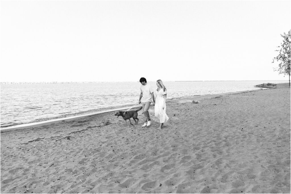 black and white photo of a couple walking down the beach with their dog