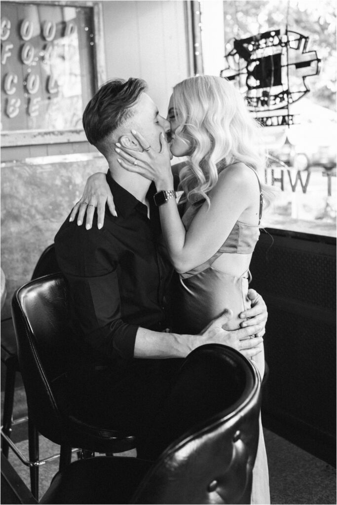 a black and white photo of a couple kissing at the bar