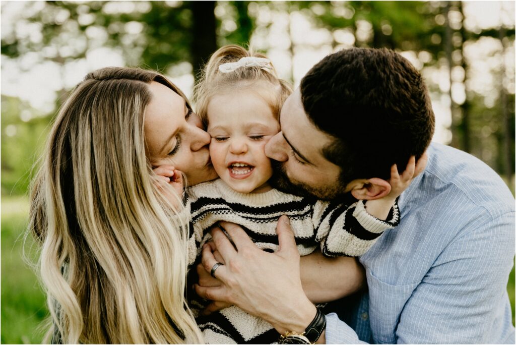 mom and dad kissing daughter on cheeks