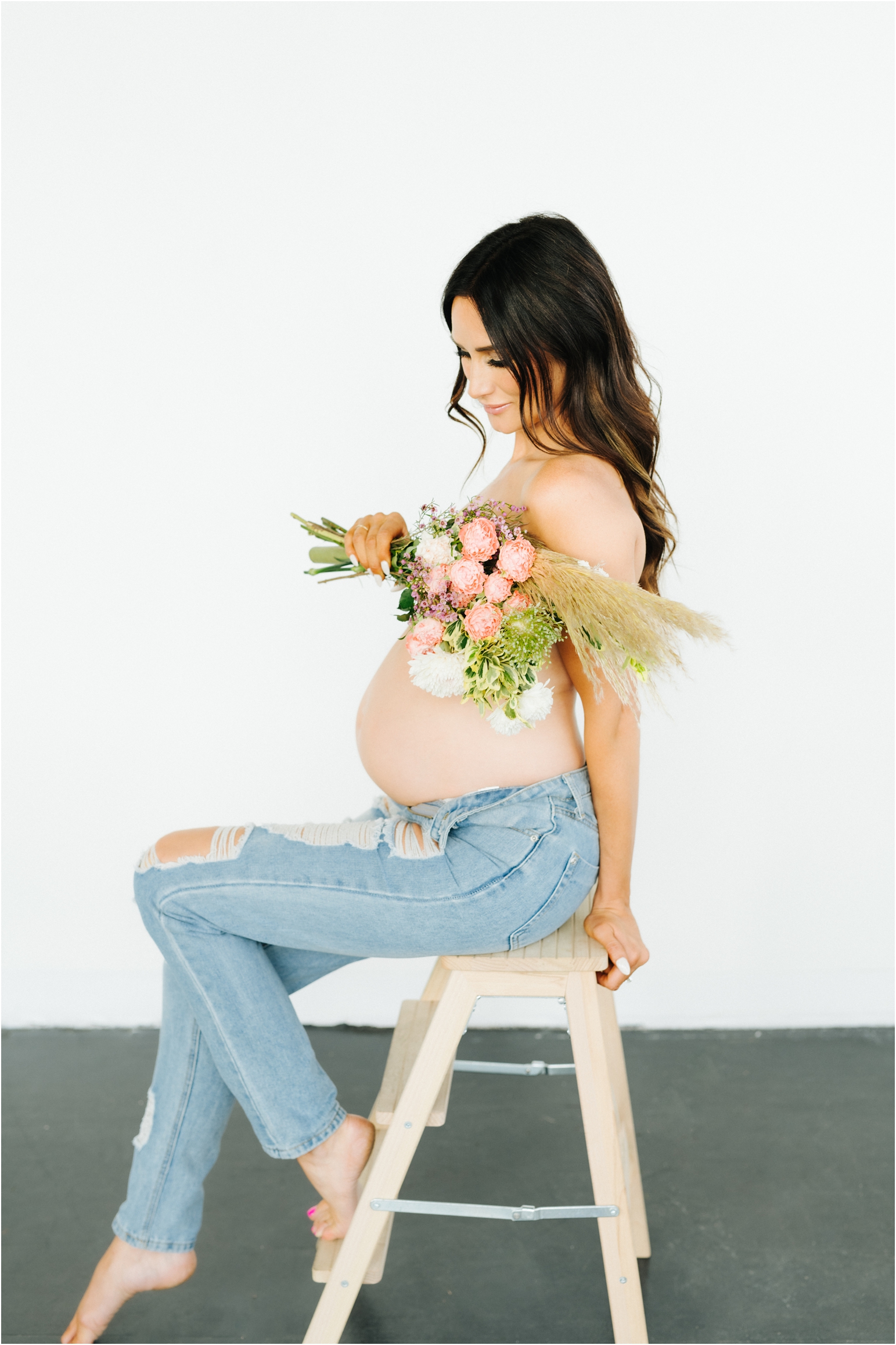 maternity photo of a woman taken in a studio with flowers and a white wall and dark floor