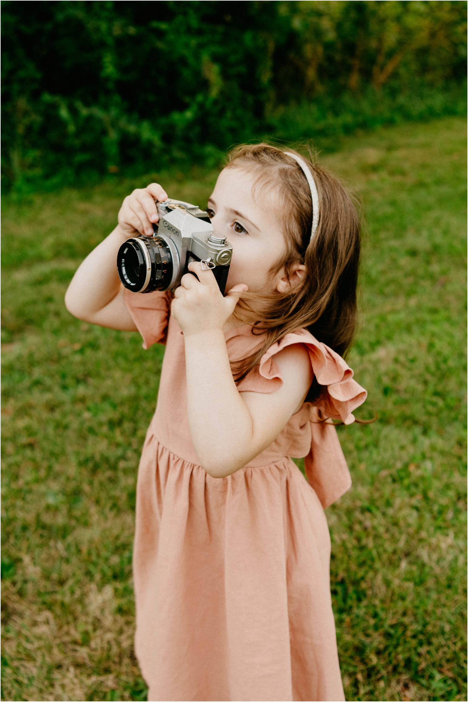 smiling toddler holding camera in pink dress