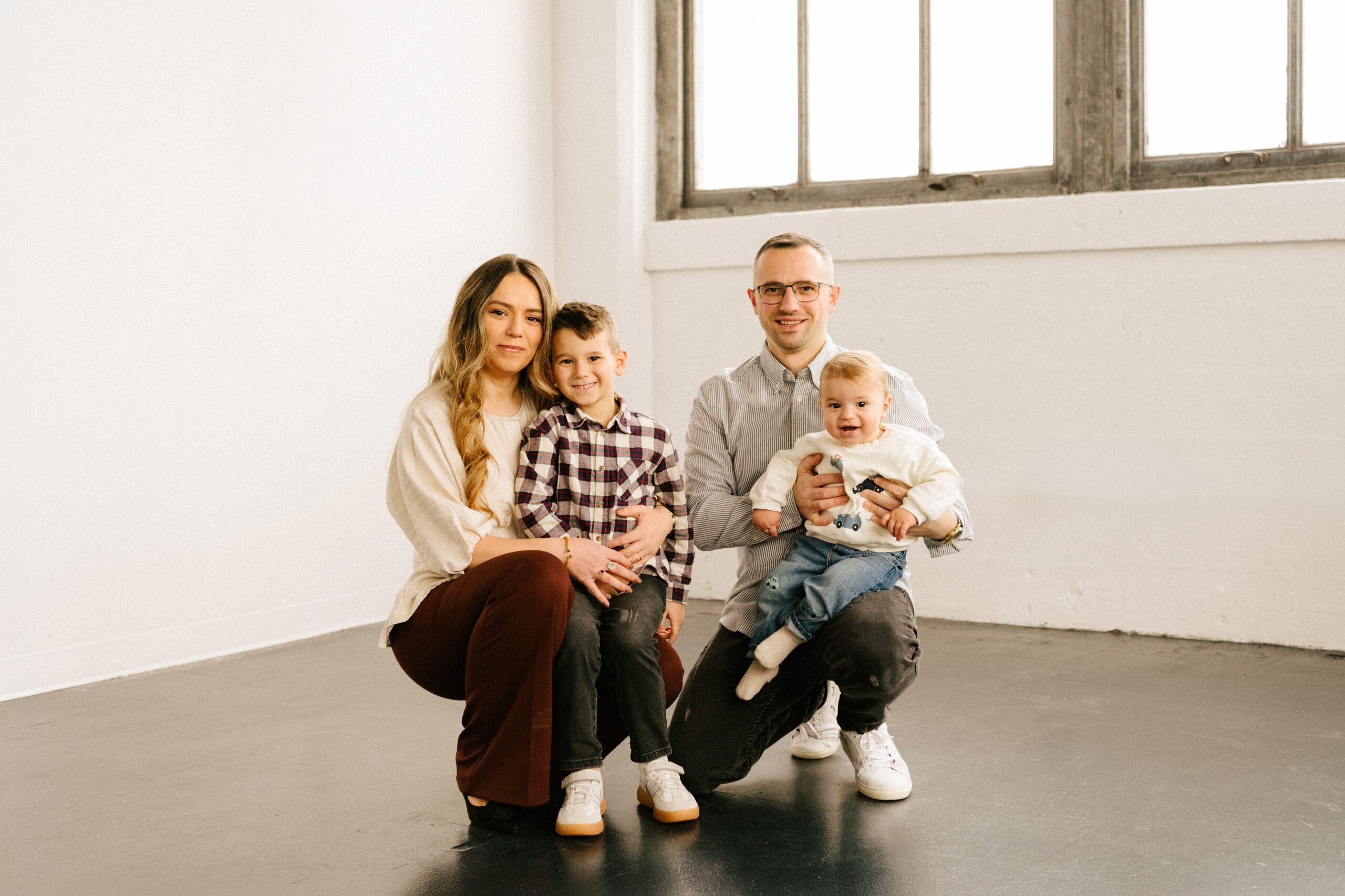 A mom, dad, and their two boys smiling in a photography studio in Milwaukee Wisconsin with natural light.