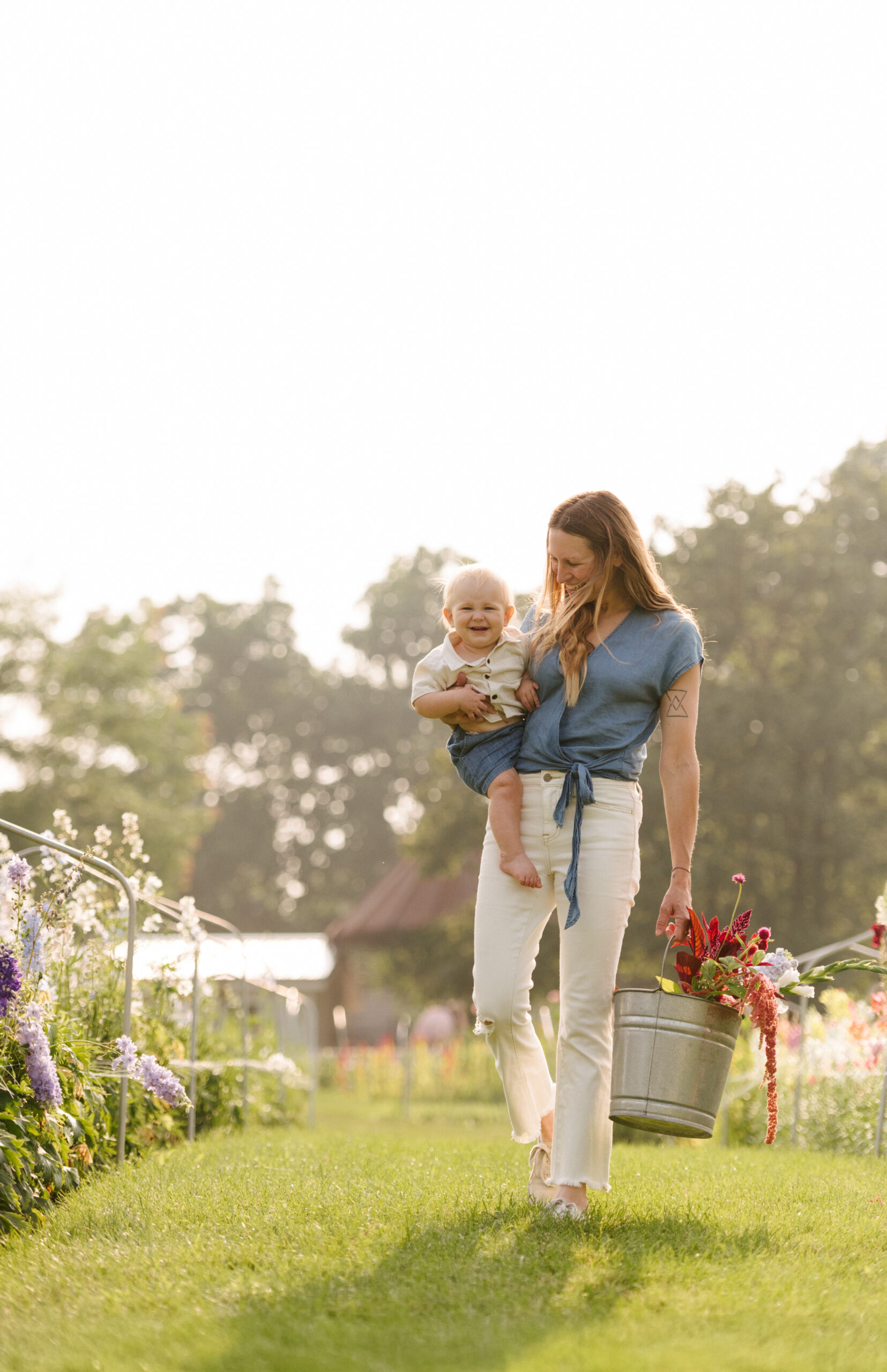 Woman holding baby in arms at flower farm in the summer.